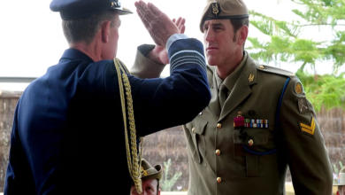 군복 차림의 벤 로버츠-스미스와 법원 또는 경찰 호송 장면을 연상시키는 이미지, 전쟁 영웅의 추락을 상징